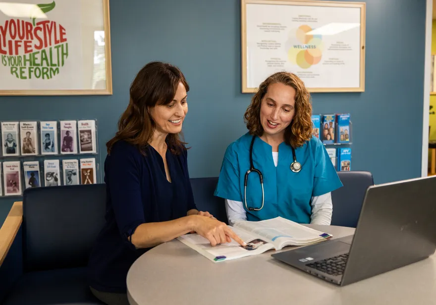 A nursing student in a scrub sitting down with a professor collaborating while looking at a textbook