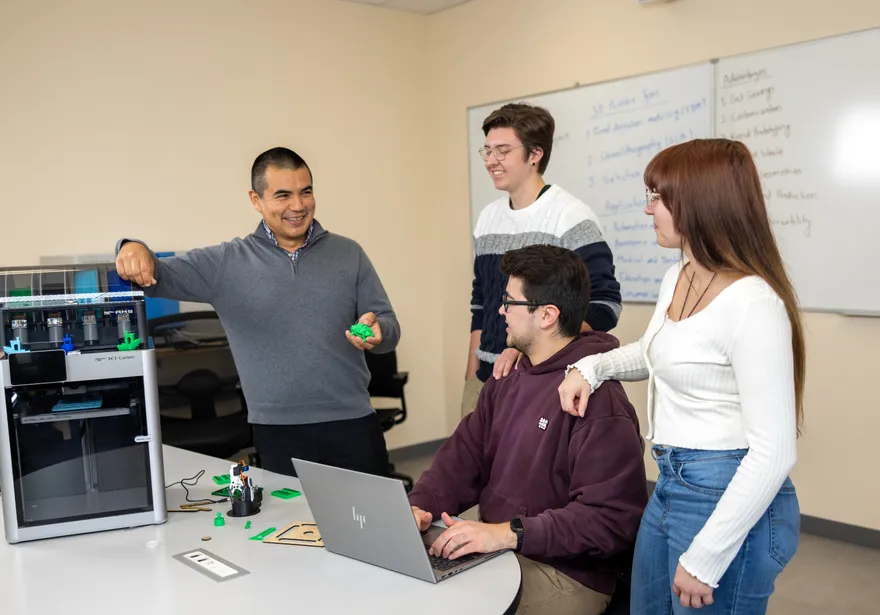 A group of four students next to a 3d printer collaborating
